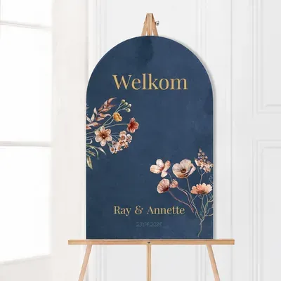 Donkerblauw boogvormig welkomstbord met droogbloemen en goudkleurige tekst op een houten ezel